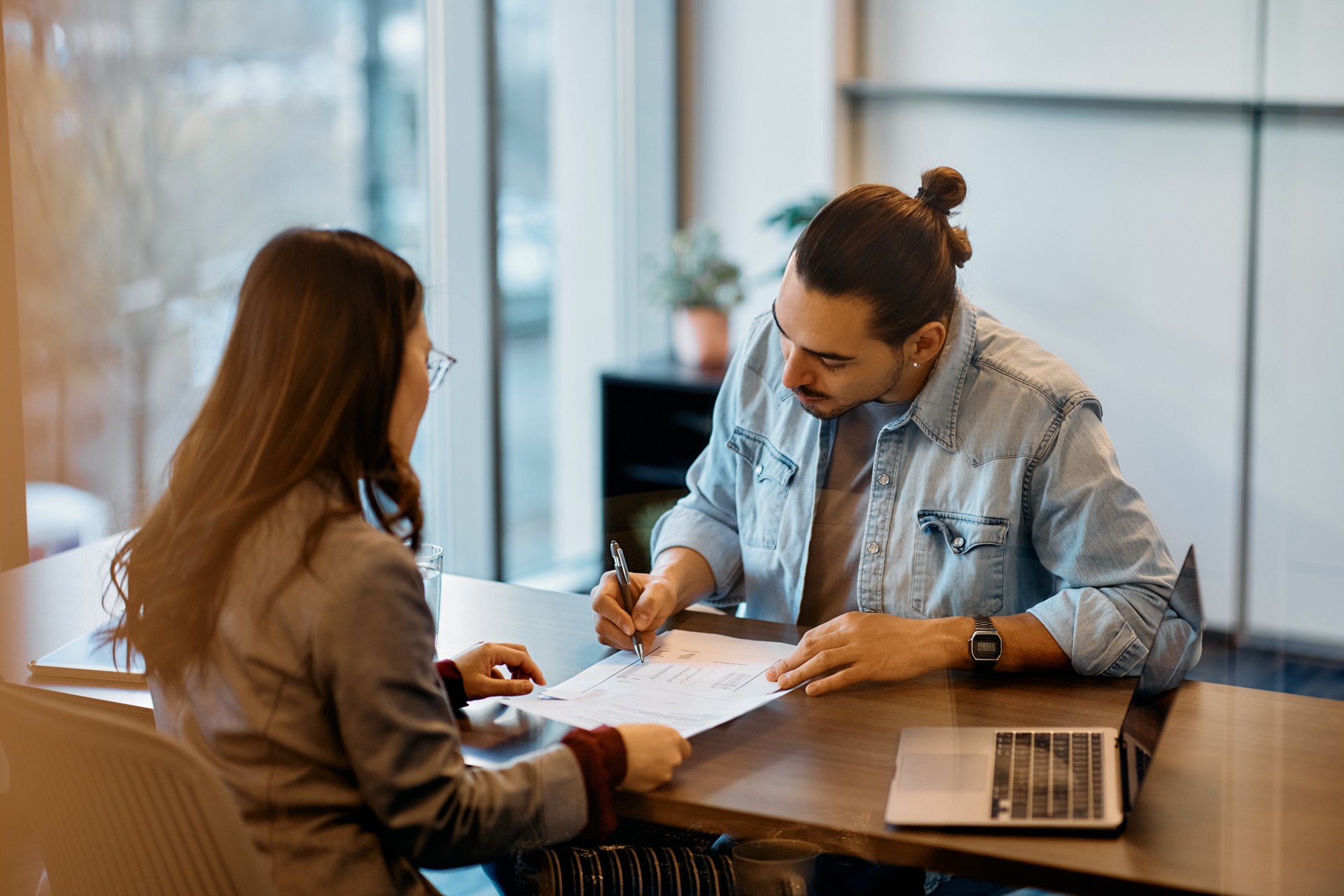 Young Hispanic man signing a loan agreement during meeting with his bank manager in the office.